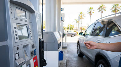 A driver refuels their car rental at a California gas station, with a sign showing cash and credit prices