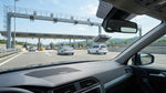 A car rental drives on a highway approaching a New York toll plaza under a clear blue sky