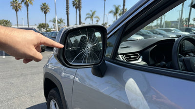 A driver inspects a cracked side mirror on a car rental in a sunny California lot