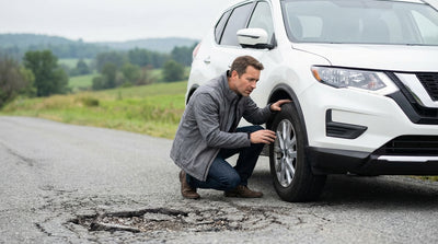 A driver inspects the front wheel of their car hire on the shoulder of a leafy road in Pennsylvania