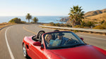 A red convertible car hire driving on a scenic coastal road in California next to the Pacific Ocean