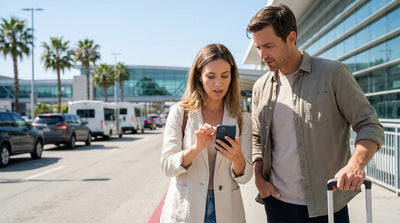 Traveler uses a smartphone in front of the LAX airport terminal before picking up their car rental in Los Angeles
