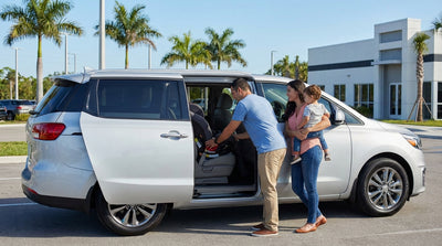 A mother fastens her child into a car seat in the back of a family car hire in sunny Florida