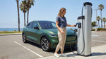 A white electric car rental is plugged into an EV charging station under sunny California palm trees
