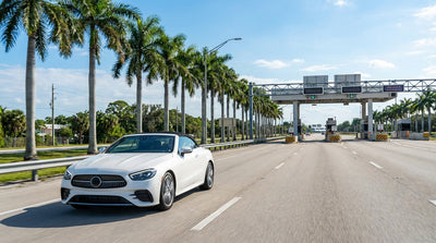 A white car hire drives under a SunPass toll gantry on a sunny highway in Florida