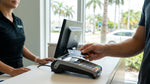 Hand tapping a contactless credit card on a payment terminal at a car hire desk in Miami