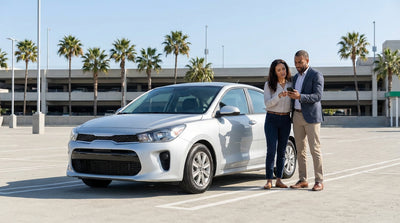 A person on a sunny street in Los Angeles looking at a smartphone next to their red car rental