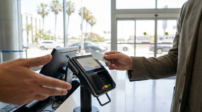 A customer at a car rental desk in Los Angeles holds a credit card over a payment terminal