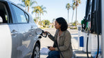 Close-up of a person pumping fuel into a car rental vehicle at a sunny gas station in California