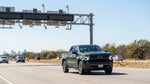 A modern car hire driving on a sunny multi-lane toll road in Texas with a toll gantry overhead