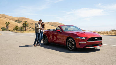 A modern car rental parked on a scenic pull-off overlooking the winding California coast at sunset