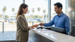 A person's hand holding a credit card at a car hire counter in a sunny Los Angeles office