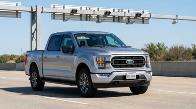 A car rental approaches an electronic toll gantry on a wide, sunny highway in Texas