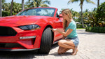 A red convertible car hire driving on Ocean Drive in Miami with palm trees and sunny skies