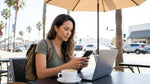 Driver using a smartphone while leaning against a white car hire vehicle on a sunny California coastal road