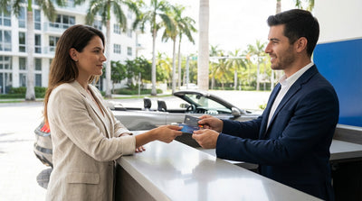 A person at a counter handing two credit cards to an agent for a car hire in Miami