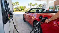 Gas pump nozzle inserted into a white car rental at a sunny Florida gas station