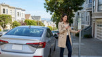 Person using a smartphone next to a car rental parked on a steep San Francisco street