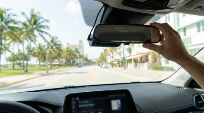 A dashcam on the windshield of a car rental in Miami captures the view of a sunny, palm-lined road