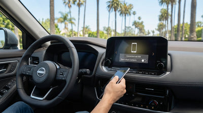 A person's hands on the wheel of a car rental driving down a sunny highway lined with palm trees in California