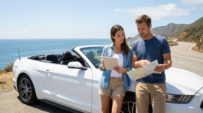 A red convertible car hire drives along a sunny, winding coastal highway in Big Sur, California