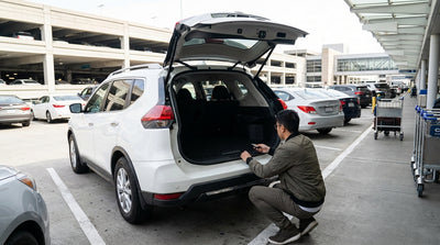 A person with luggage stands by the closed trunk of their car hire sedan at a JFK Airport parking lot in New York