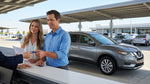 A traveler inspects their car hire vehicle in a multi-level parking garage at a busy US airport