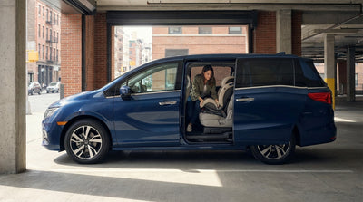 A parent installs a child car seat into the back of a car hire vehicle on a street in New York City