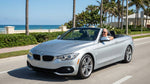 An older couple smiles next to their convertible car hire on a sunny palm-lined road in Florida