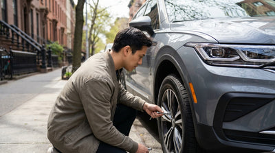 A driver inspecting the wheel of a car rental vehicle parked on a street in New York