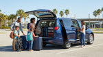 Family of five loading luggage into a spacious car rental SUV parked under palm trees in Florida