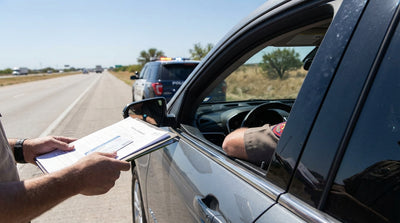 A police car with flashing lights has stopped a car hire on the shoulder of a dusty Texas road