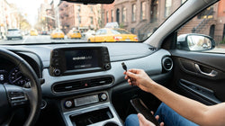 Phone connected to a car rental dashboard via USB cable with a New York street view through the front windshield