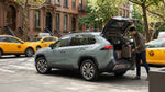 A person loads luggage into the trunk of a car hire parked on a busy street in New York City