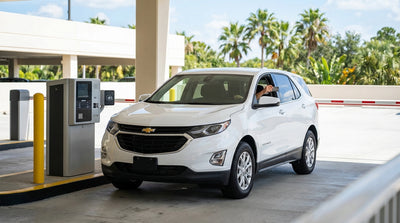 A white car rental drives under the iconic Walt Disney World entrance archway in Orlando, Florida