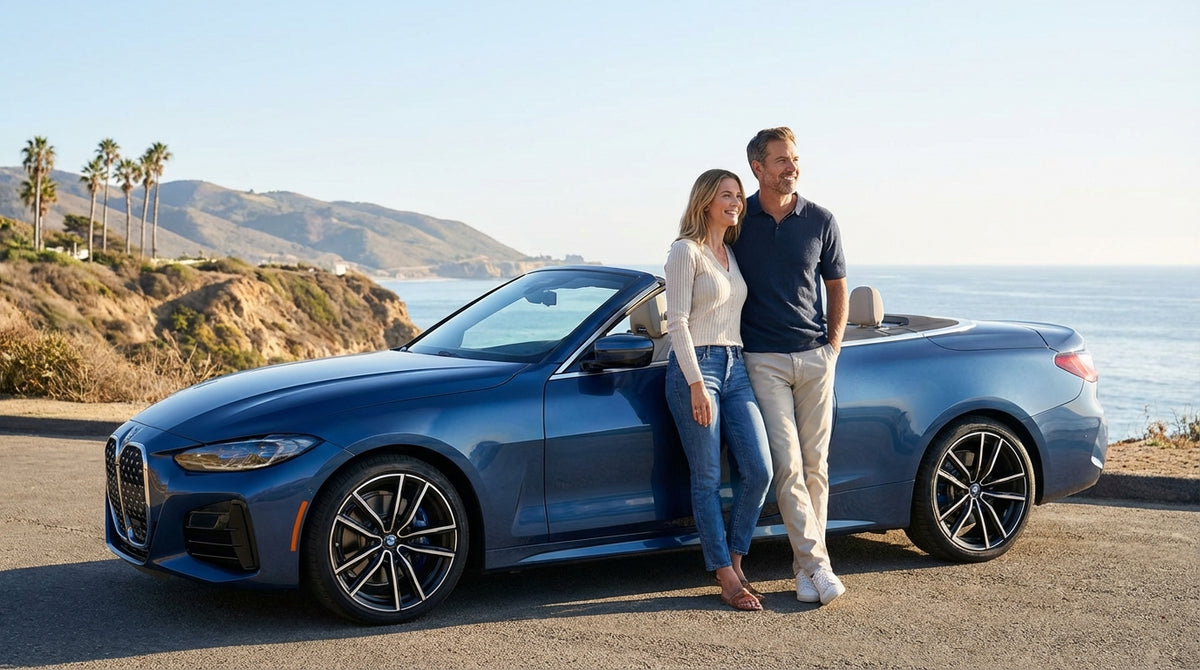 A couple smiles in a convertible, enjoying their car hire drive along a sunny California coastline
