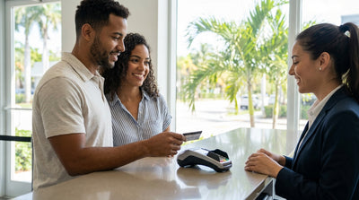 Hand holding a credit card and keys for a car hire on a sunny, palm-lined street in Miami