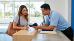 A person hands their passport to an agent at a car rental desk in a sunny California airport