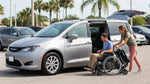 A person loading a folded wheelchair into the trunk of a spacious car rental SUV parked in Orlando