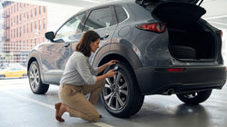 Person crouching to inspect the front tire of a car rental parked on a New York street