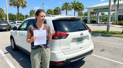 A white car hire driving on a sunny highway lined with palm trees in Florida