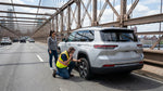 A New York car hire vehicle with a flat tyre stopped on the shoulder of a bridge overlooking the city skyline