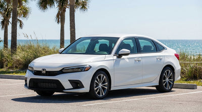 A silver car rental driving on a coastal road next to a turquoise ocean and palm trees in Florida