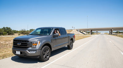 A driver holds a smartphone with Google Maps open inside their car rental on a sunny Texas highway