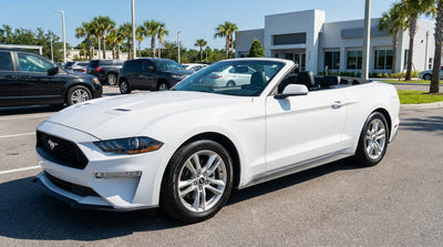 A white convertible car rental driving down a sunny coastal highway lined with palm trees in Florida