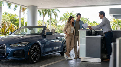 A convertible car hire drives down a sunny street in Miami lined with palm trees and colorful Art Deco buildings