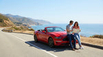 A convertible car rental parked on a Highway 1 viewpoint overlooking the Bixby Bridge in Big Sur, California