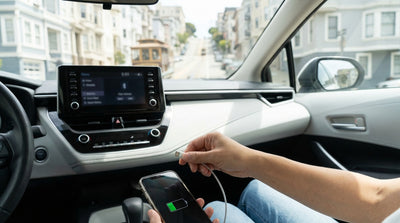 A person charging a smartphone in a car rental with the San Francisco skyline visible through the windshield