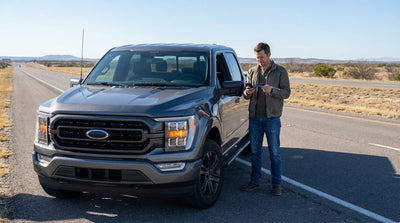 A driver on their phone next to their broken-down car hire on the shoulder of a hot Texas highway