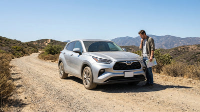 A white car rental drives down a winding, unpaved road in the dusty California hills
